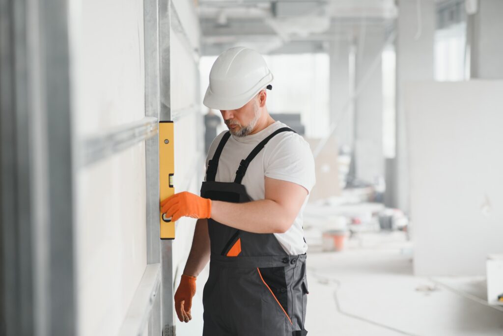 Man holding level against plasterboard, interior drywall. Attic renovation