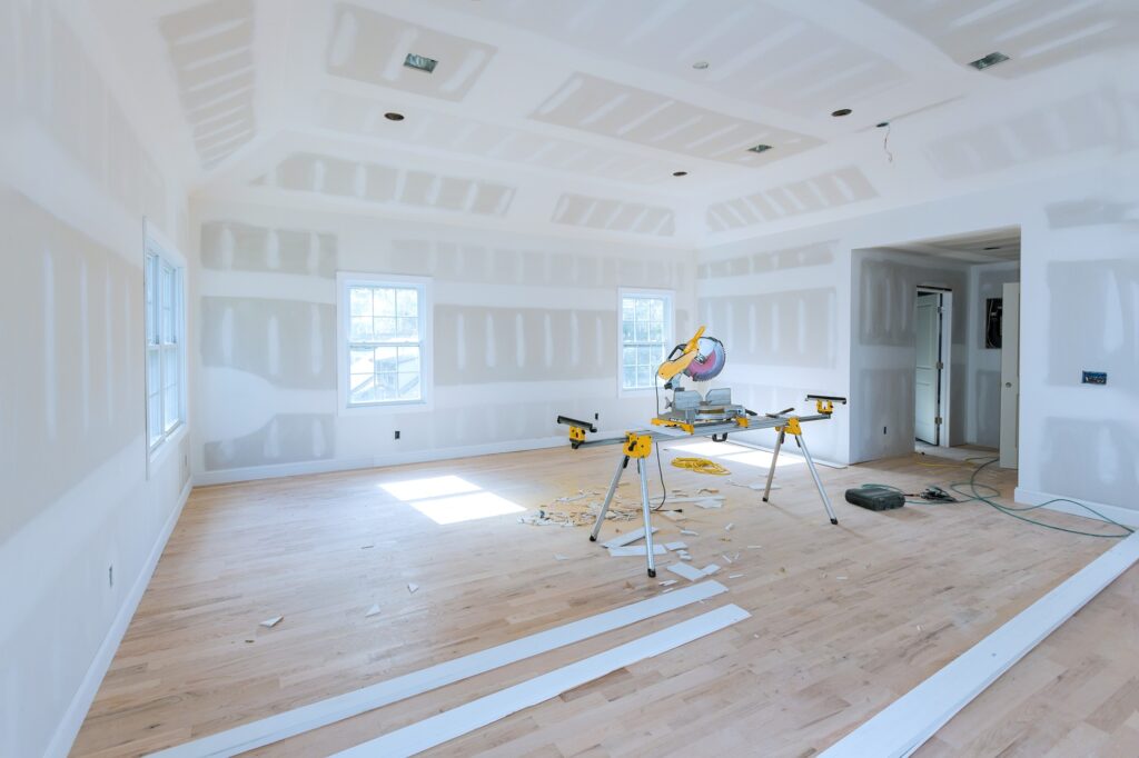Spacious, unfinished room with drywall partially installed miter saw set up in center on stand